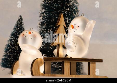 Scheda di Natale, il giocattolo pupazzi di neve (ornamenti) su una slitta avente il divertimento di fronte degli alberi di Natale. Foto Stock