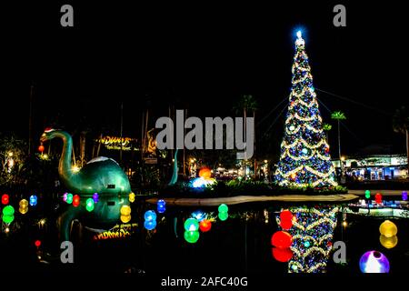 Orlando, Florida. Novembre 27, 2019. Grande dinosauro, albero di Natale e decorazioni vacanze nel lago di eco agli Studios di Hollywood Foto Stock