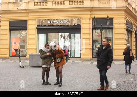 Due giovani donne (18-24 anni) guardando un telefono cellulare al di fuori del negozio Swarovski a Praga, Repubblica Ceca. Dicembre 2019. Foto Stock