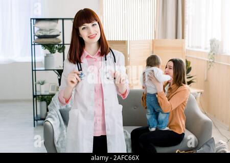 Medicina, sanità, pediatria e concetto di persone - donna medico in camice bianco e con stetoscopio paziente in visita a casa. Carino bambina con il suo Foto Stock