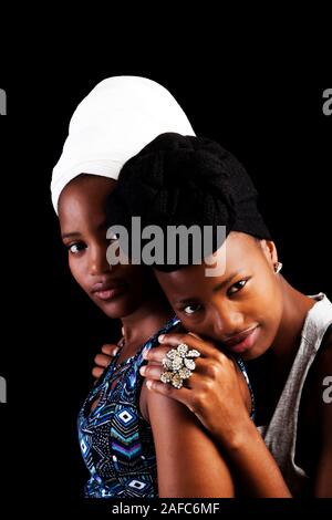 Due giovani attraenti americano africano Donna vestita di nero e bianco Headscarfs su sfondo scuro Foto Stock