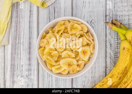 Fatte fresche Banane essiccate chip su un vecchio e rustico tavolo in legno; messa a fuoco selettiva; close-up shot Foto Stock
