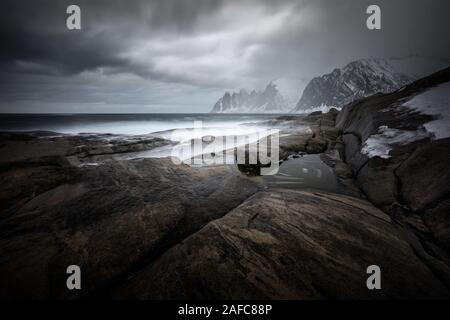 Tugeneset costa rocciosa con le montagne sullo sfondo durante le tempeste, Norvegia Foto Stock