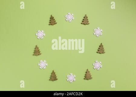 Composizione di natale. Ghirlanda di Natale fatto di piccoli alberi di natale e i fiocchi di neve su sfondo verde. Appartamento laico, vista dall'alto, copia dello spazio. Foto Stock