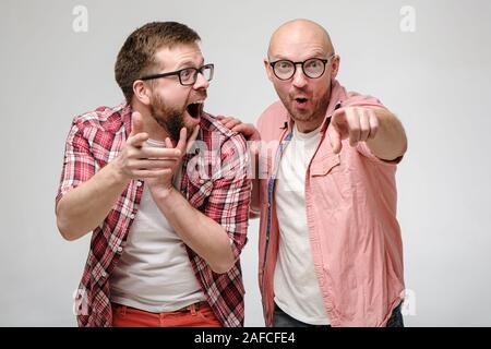 Divertente di uomini in bicchieri punto a qualcuno con le loro mani, sono sorpreso che cosa hanno visto, sono felici e ridere a voce alta. Foto Stock