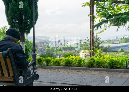 Un solitario vecchio seduto su una panchina in un parco a Tbilisi tra colorate alberi d'estate. Foto Stock