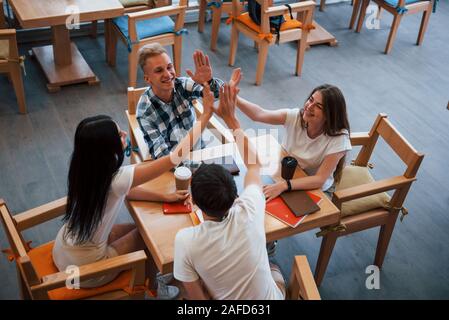 Seduto nella caffetteria e una conversazione. Quattro giovani studenti in abiti casual sono riuniti a Rainy day Foto Stock