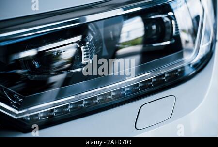 Parte anteriore del moderno nuovo di zecca bianco auto. Parcheggiato a showroom. La riflessione dei fari anteriori Foto Stock