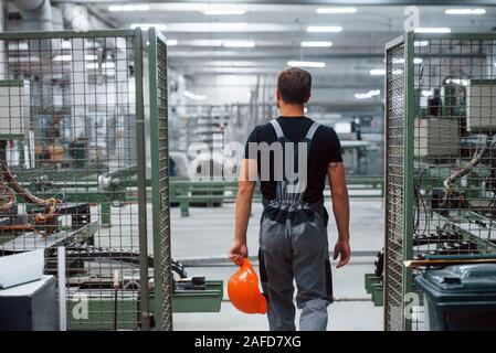 Operaio industriale in ambienti interni in fabbrica. Giovane tecnico con orange elmetto Foto Stock