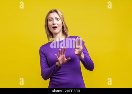 Ho paura! Ritratto di panico paura donna in stretto vestito viola alzando le mani, guardando la fotocamera con inorridito gli occhi e la bocca aperta, improvviso spavento Foto Stock