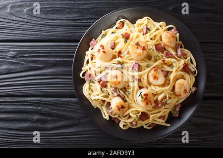 Spicy spaghetti servita con capesante e bacon in crema salsa al formaggio close-up in una piastra sul tavolo. parte superiore orizzontale vista da sopra Foto Stock