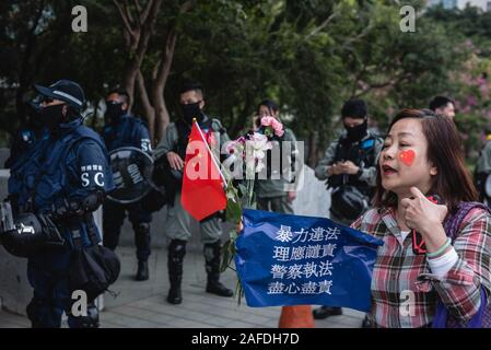 Un pro-government protester passeggiate passato poliziotti tenendo una bandiera cinese, cartellone e fiori durante il rally.Migliaia di pro-governo manifestanti radunati per gridare slogan, wave bandiere e cartelli portano a sostegno della polizia di Hong Kong ha nella loro manipolazione delle proteste che hanno afflitto di Hong Kong per gli ultimi 6 mesi. Foto Stock