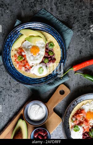 Deliziosa Huevos Rancheros Tostadas, colazione messicana consistente di tortilla tostato, pomodoro tagliato a pezzetti e la cipolla, jalapeno e fagiolo mash, guarnita con f Foto Stock
