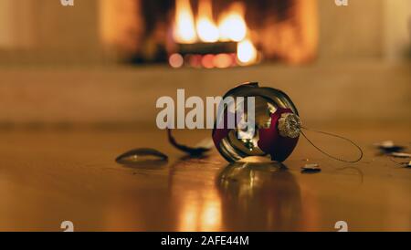Pallina di natale rotto. Pallina di natale si è schiantato giù sul pavimento di legno. Vacanze di Natale sfondo, blur caminetto Foto Stock