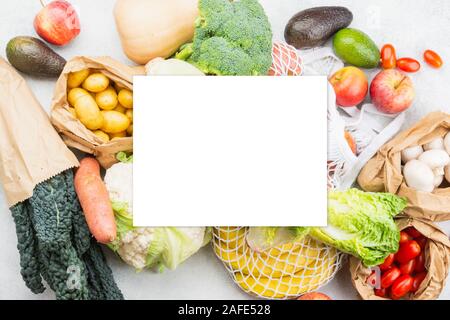 Assortimento di frutta verdura riutilizzabili in maglia bianca, cotone e sacchi di carta bianca sul tavolo da cucina, vista dall'alto, il fuoco selettivo. Libro bianco sulla parte superiore, copia spazio per il testo Foto Stock