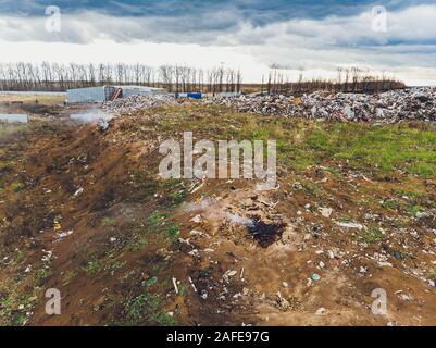 La grande heap dump di rifiuti si estende parallelamente al fiume,Garbage montagne con cielo nuvoloso di massa indietro in giorno luce,rifiuti ha prodotti petroliferi sono Foto Stock