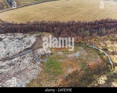 La grande heap dump di rifiuti si estende parallelamente al fiume,Garbage montagne con cielo nuvoloso di massa indietro in giorno luce,rifiuti ha prodotti petroliferi sono Foto Stock