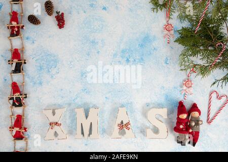 Little dwarf bambole sono seduti sulle scale di Natale. Le decorazioni di Natale in legno per lettere XMAS su un blu e sfondo bianco Foto Stock