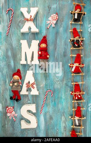 Little dwarf bambole sono seduti sulle scale di Natale. Rosso Natale decorazioni in legno per lettere XMAS Foto Stock