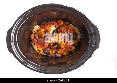Vista superiore del pollo arrosto con albicocche e prugne secche e date in un buio pentola di creta su sfondo bianco. Foto Stock