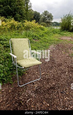 Olg verde giallo sedia pieghevole in un luogo solitario sulla riva del lago Ammersee in Baviera, invitando a sedersi ma purtroppo bagnato Foto Stock