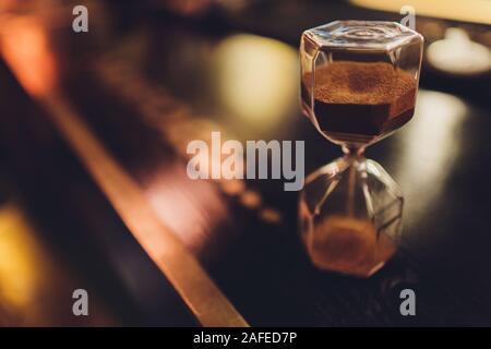 Clessidra con sabbia in caduta all'interno di un bulbo di vetro, del passare del tempo o tempo perso su sfondo scuro con spazio per il testo Foto Stock