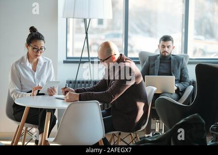 Gruppo di dialogo interculturale occupato co-lavoratori nel convenzionale lavora nella lounge dell'hotel Foto Stock