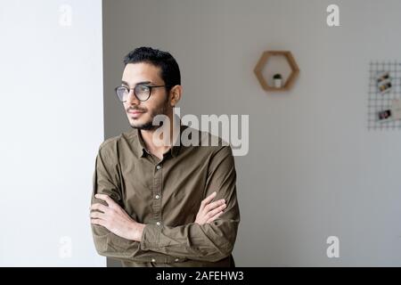 Giovani cross-imprenditore armati in occhiali e camicia guardando attraverso la finestra Foto Stock