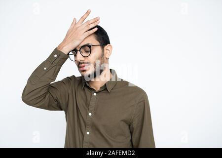 Imbarazzato proprietario in occhiali mantenendo la mano sulla fronte in isolamento Foto Stock