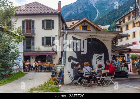 Una famiglia mangia la cena ad un tavolo di cui al di fuori di un ristorante Chamonix con un dipinto sulla parete. Foto Stock