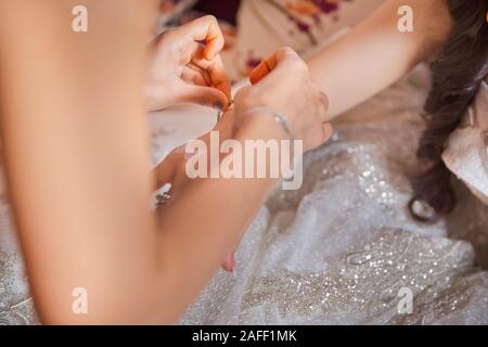 Sposa la messa sui gioielli, focus sul bracciale. Close up di groom dando la sua sposa bracciale come simbolo del suo amore il loro giorno delle nozze . Damigella aiuta a Foto Stock