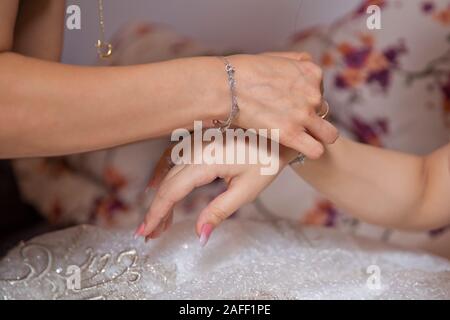 Sposa la messa sui gioielli, focus sul bracciale. Close up di groom dando la sua sposa bracciale come simbolo del suo amore il loro giorno delle nozze . Damigella aiuta a Foto Stock
