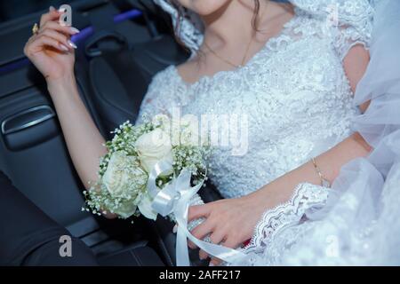La sposa indossa pantaloni bianchi . La sposa si sedette nella sua auto e mettere la mano sul bianco fiore di nozze . Foto Stock