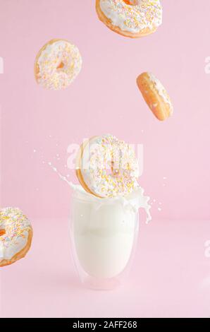 Le ciambelle glassate al spruzza rientranti nel vetro di schizzi di latte sulla rosa pastello sfondo. Flying food concept. Foto Stock