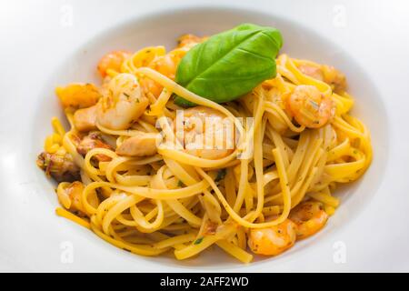 Tagliatelle con gamberi in salsa di erbe su una piastra bianca decorata con foglie di basilico Foto Stock