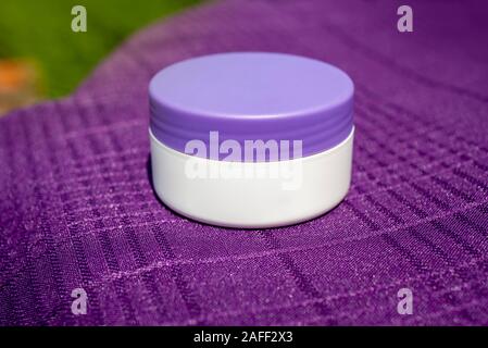 Crema cosmetica contenitore foto scattata al di fuori con la luce del sole mettere sul tessile viola ametista con coperchio Foto Stock