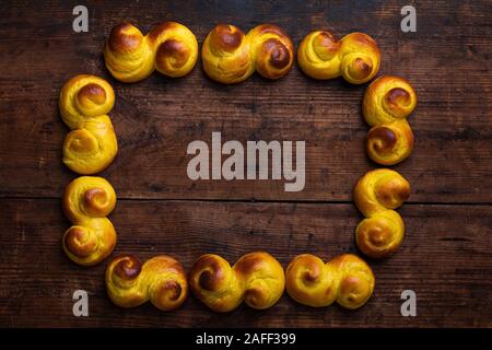 Tradizionale svedese bun natale Lussekatter Lussebullar o su una tavola in legno rustico, in forma di un telaio con una copia dello spazio. Le ciambelle sono appena m Foto Stock