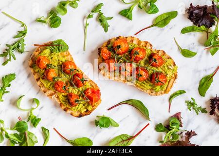 Brinda con purea di avocado guacamole ed essiccati in forno i pomodori ciliegia. Le due fette biscottate sono visti da sopra il piano prospettiva laica e ci sono lasciare insalata Foto Stock