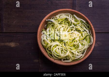 Zoodles zucchine tagliatelle spiralizzato sano piatto di verdure in una ciotola di legno, al buio su un tavolo di bambù. Visto da sopra il piano si coricò con copia spazio. Foto Stock