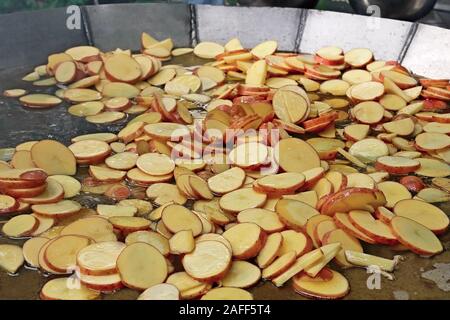 Un sacco di forma arrotondata a fette fette di patate fritte sono in metallo grandi fatti a mano la coppa in acciaio in olio bollente all'aperto Foto Stock