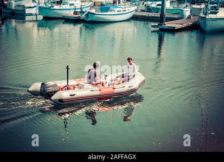 Un giovane uomo manzi il gommone mentre l'altro giovane rivolto all'indietro nell'imbarcazione al Santa Barbara harbour marina, Santa Barbara, CA, Stati Uniti d'America Foto Stock