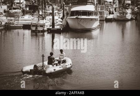 Un giovane uomo manzi il gommone mentre l'altro giovane rivolto all'indietro nell'imbarcazione al Santa Barbara harbour marina, Santa Barbara, CA, Stati Uniti d'America Foto Stock