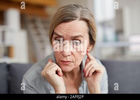 Ritratto di triste donna matura seduti sul divano di casa e guardando lontano con preoccupazione e ansia, spazio di copia Foto Stock