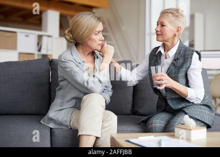 Ritratto di femmina matura psicologo comporting senior paziente e offrendo un bicchiere di acqua durante la sessione di terapia, spazio di copia Foto Stock