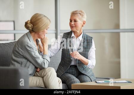 Ritratto di cura psicologo femmina che offre un bicchiere di acqua per piangere donna senior mentre la sua consolante durante la sessione di terapia, spazio di copia Foto Stock