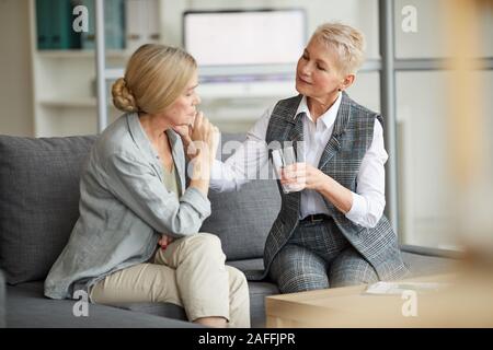 Ritratto di cura psicologo femmina che offre un bicchiere di acqua alla donna senior mentre la sua consolante durante la sessione di terapia, spazio di copia Foto Stock