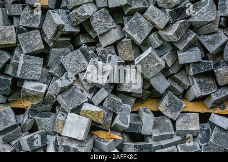 Pila di nera pietra naturale cubi per rendere pavimento esterno di piastrelle. Cataste caotiche di rotture di piastrelle su strada. Costruzione sullo sfondo di un pasticcio bac geometrica Foto Stock