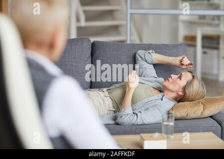 Vista laterale ritratto di piangere donna matura sdraiato sul lettino e parlando di psicologo femmina durante la sessione di terapia, spazio di copia Foto Stock