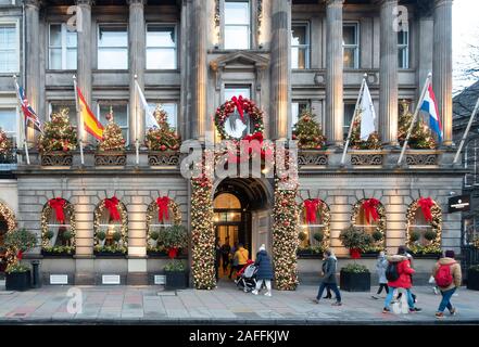 Le persone che lasciano, inserendo e facendo passare l'InterContinental Hotel su George Street nel centro di Edimburgo, in Scozia. La parte anteriore dell'hotel è decorato per il Natale con alberi di Natale sui balconi, una grande corona sopra la porta, e ghirlande con rosso e oro e baubles red ribbon. Foto Stock