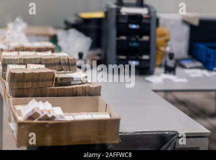 Grande quantità di contanti divisi e ordinati con bande di valuta e posti in scatole di cartone nella parte anteriore del dispositivo di conteggio Foto Stock